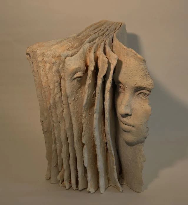 A carved face emerging from layered stone leaves