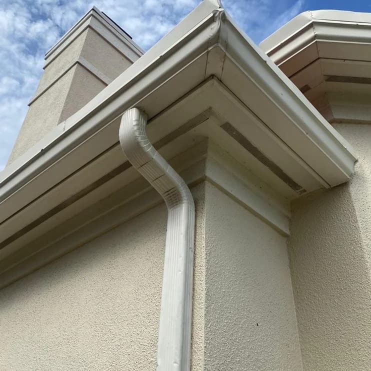 A white gutter and downpipe against a blue sky