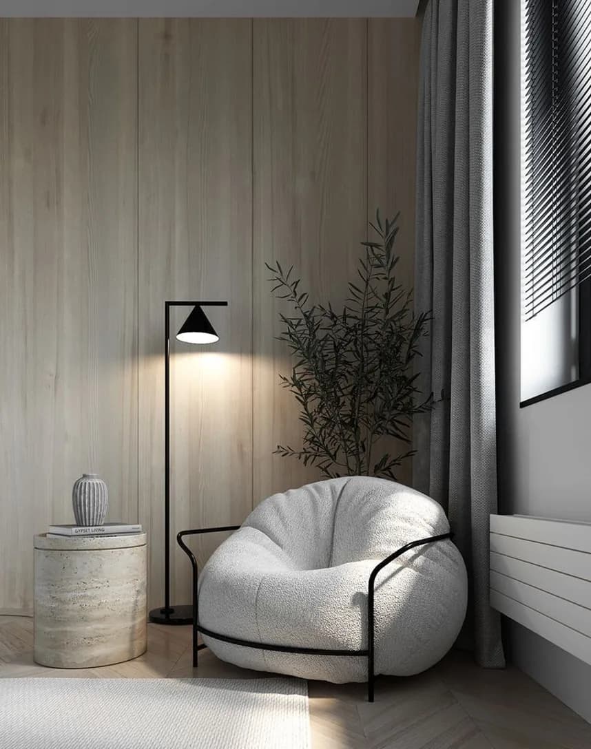 A round upholstered chair by a window under a floor lamp