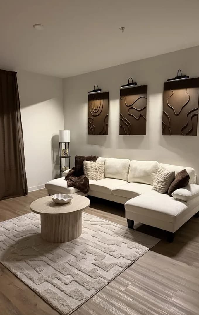 A cream sofa and round table under a row of framed prints