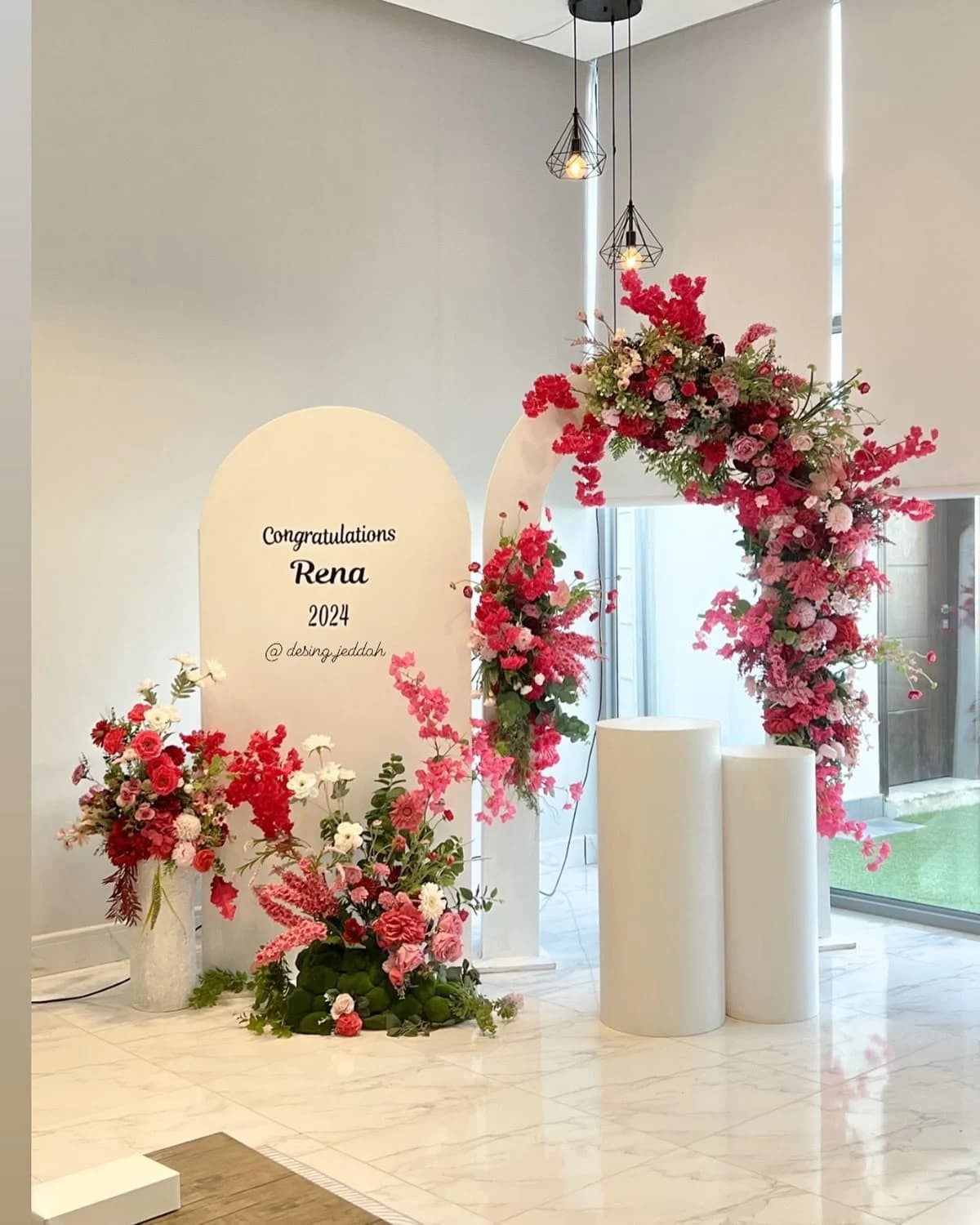 A congratulations backdrop of red and pink blooms around an arched mirror