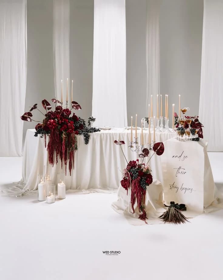 A white styled table dressed with dark red anthuriums and candles