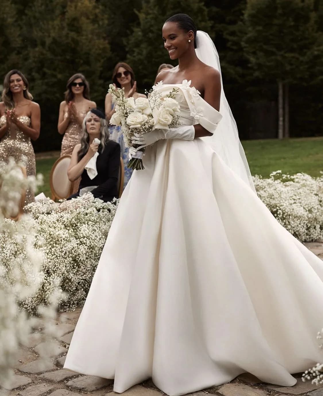 A bride carrying a white bouquet through a gypsophila-lined garden