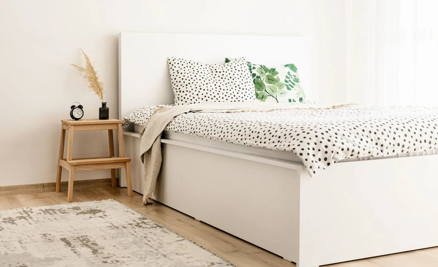 A made bed in spotted linen beside a wooden step stool