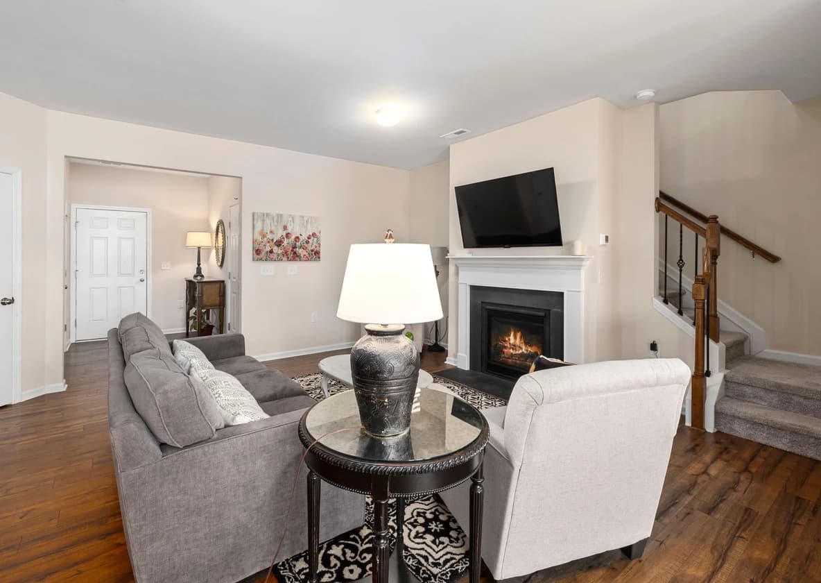 A living room with a pale sectional, a glass side table and a lit fireplace