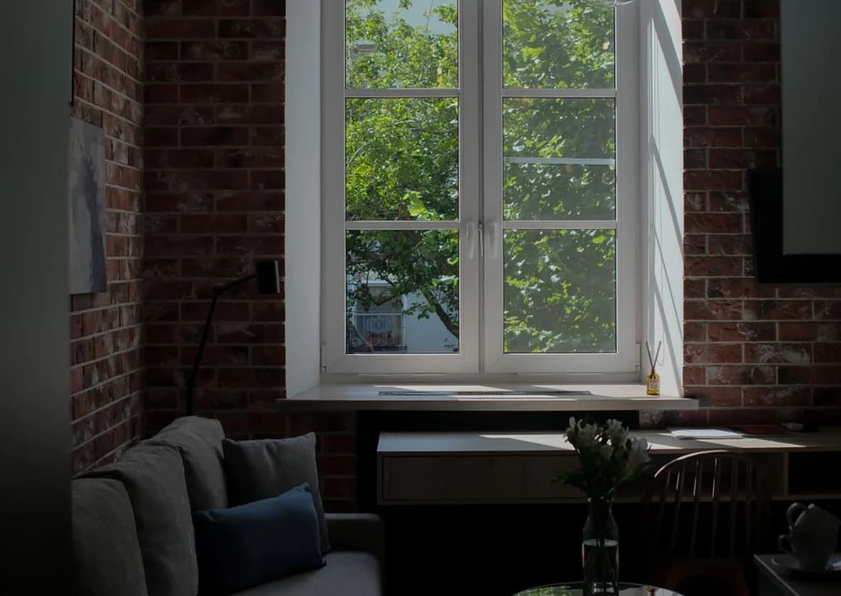 A brick-walled room with tall sash windows over a low daybed