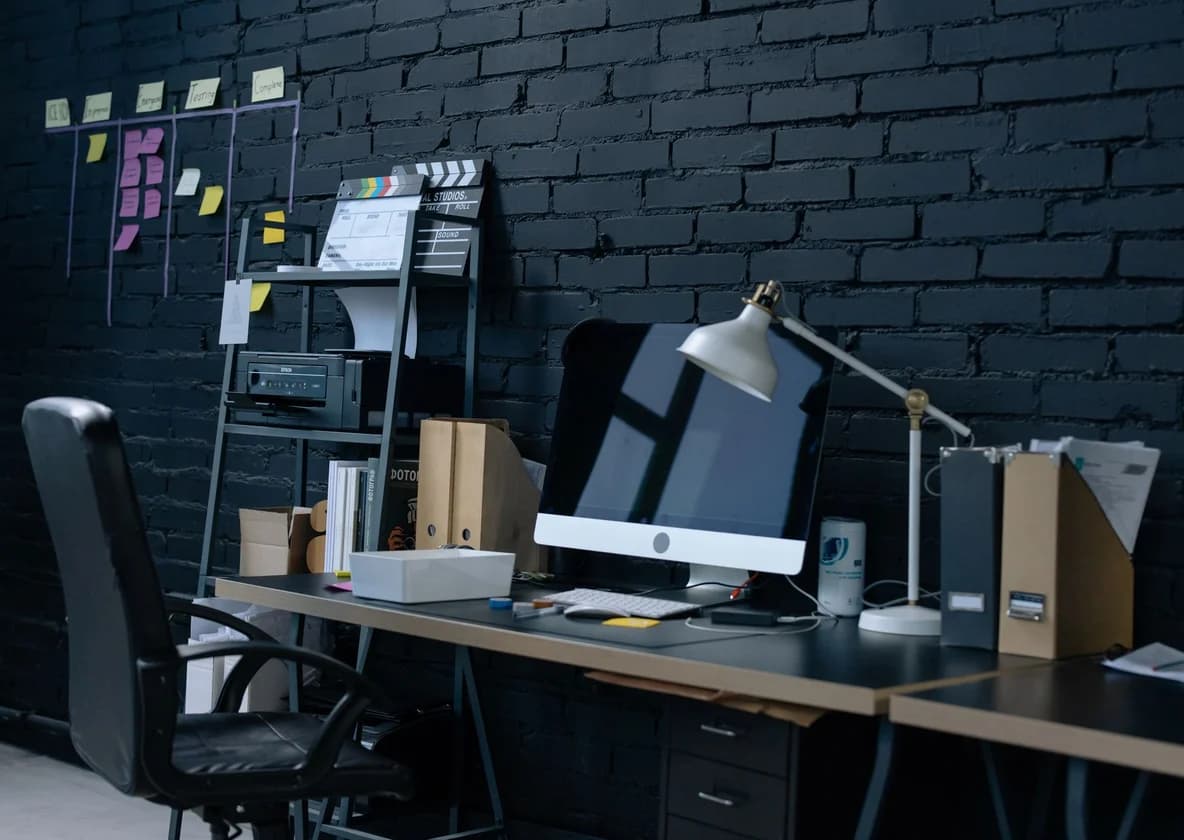 A dark brick study with a long desk, task lamp and pinned notes