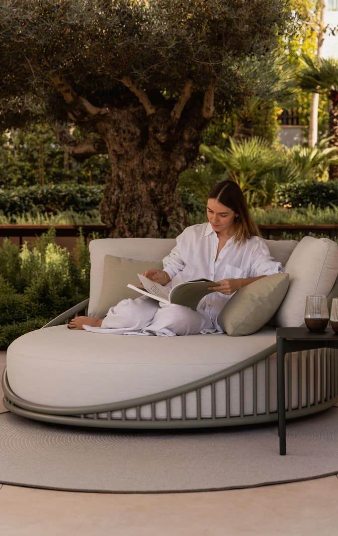 A reader on a woven garden daybed at dusk