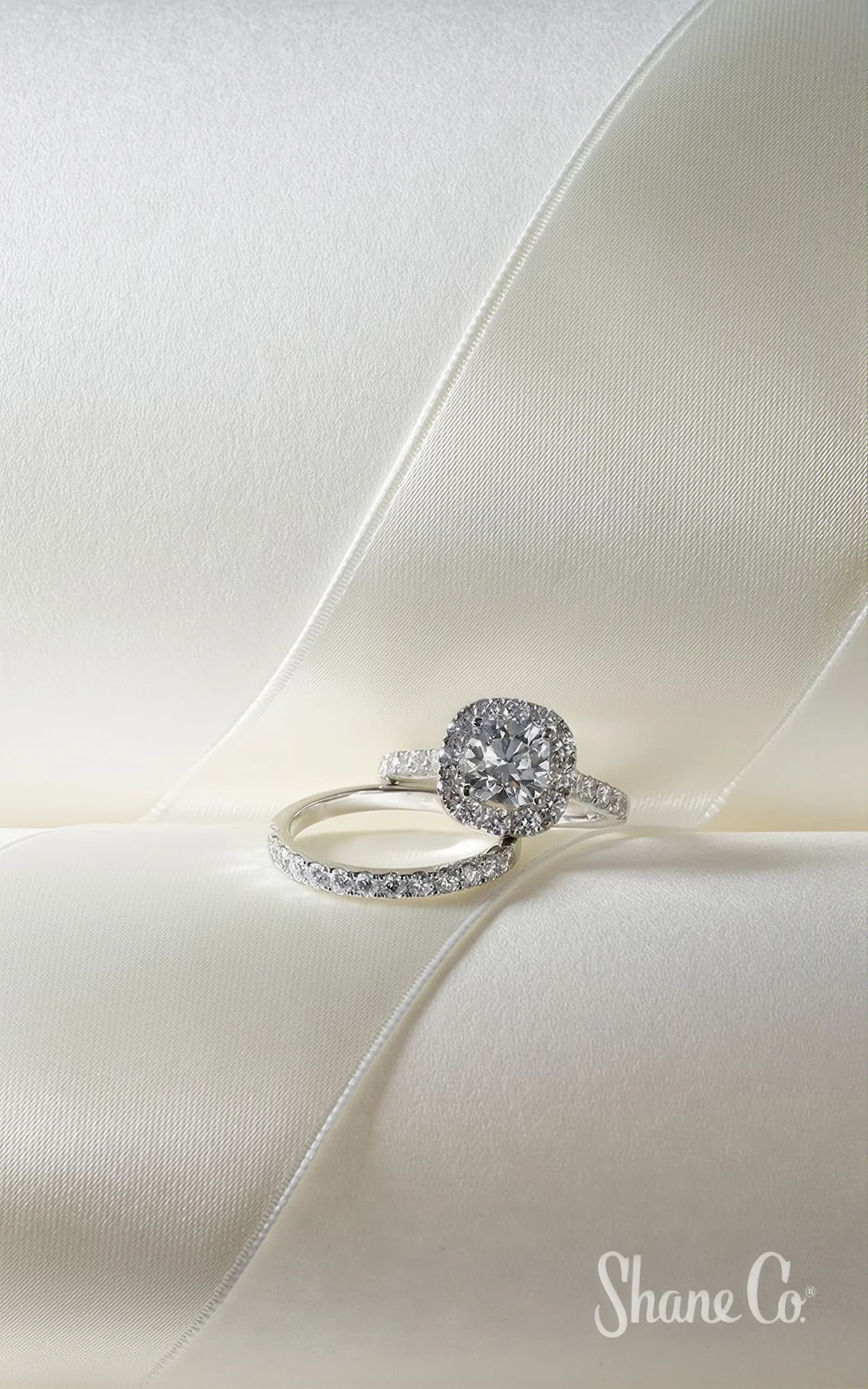 A cushion-cut halo ring and its pave band on ivory silk