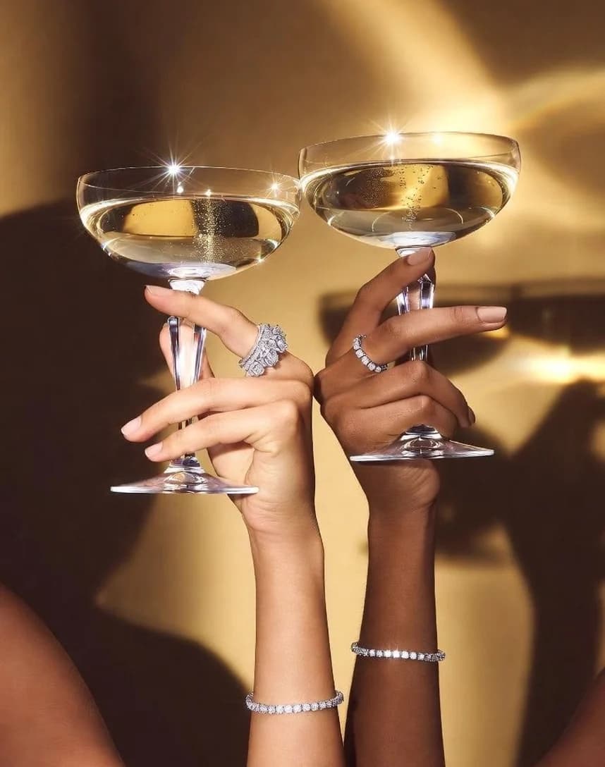Two hands raising coupe glasses under a warm light