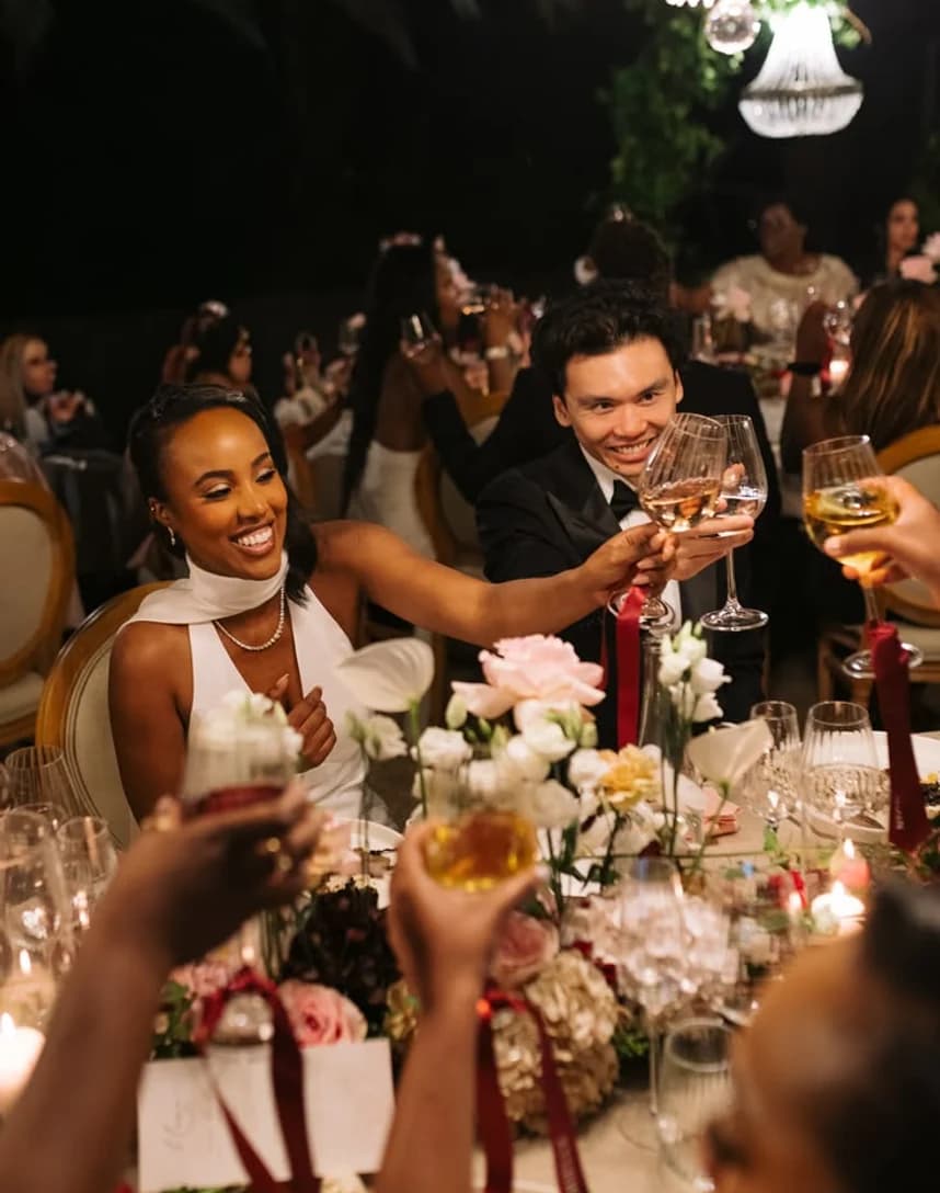 A long candlelit table of guests toasting over flowers