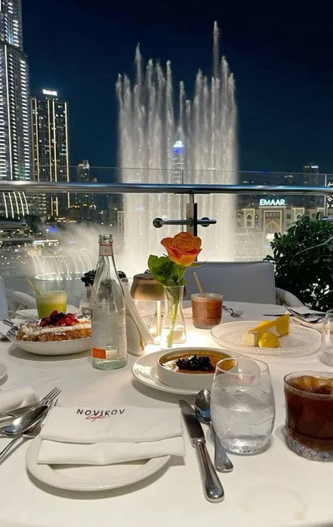 A laid dinner table on a terrace above a lit fountain