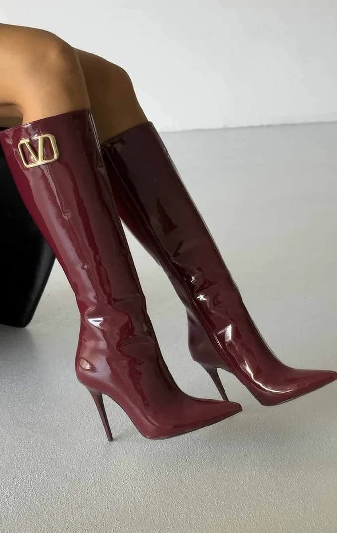 Burgundy patent knee boots against a pale studio wall