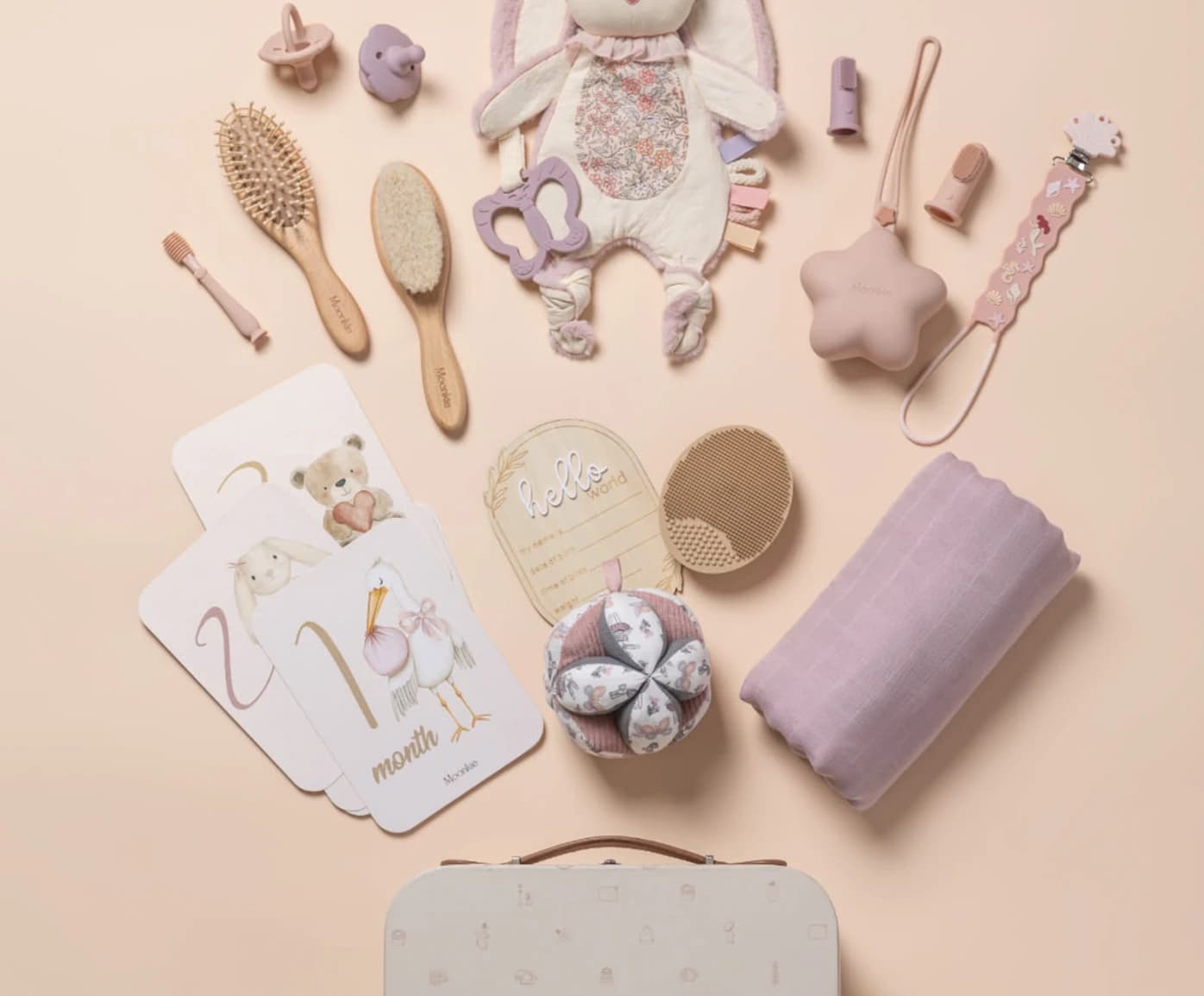 A flat-lay of newborn clothes, a brush set and a lilac blanket