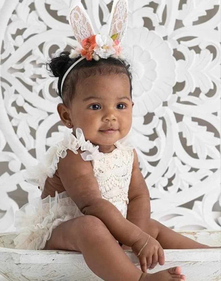 A baby in a white dress and a bunny-ear headband