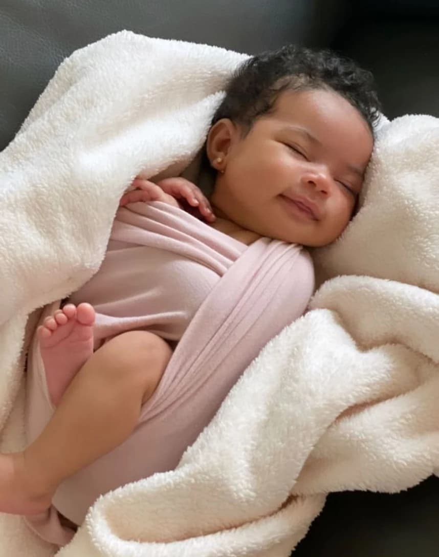 A newborn swaddled in pink on a cream blanket