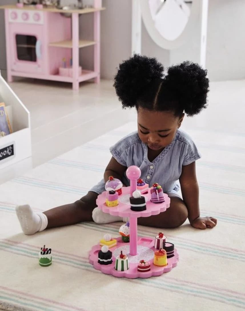 A toddler playing at a pink toy kitchen
