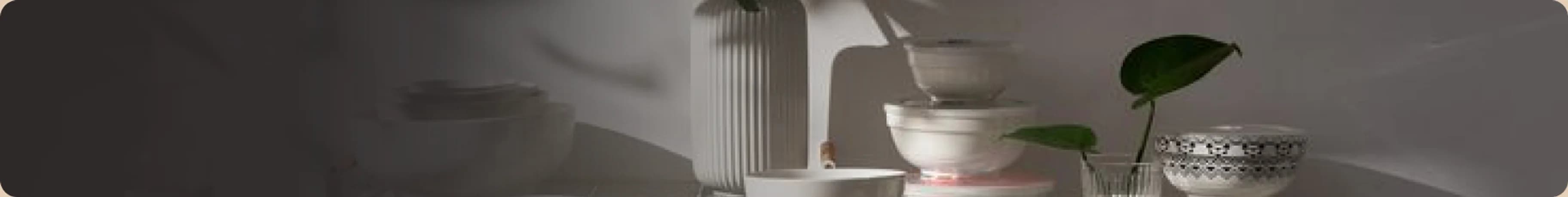 Stacked ceramic bowls and a fluted vase on a sunlit shelf