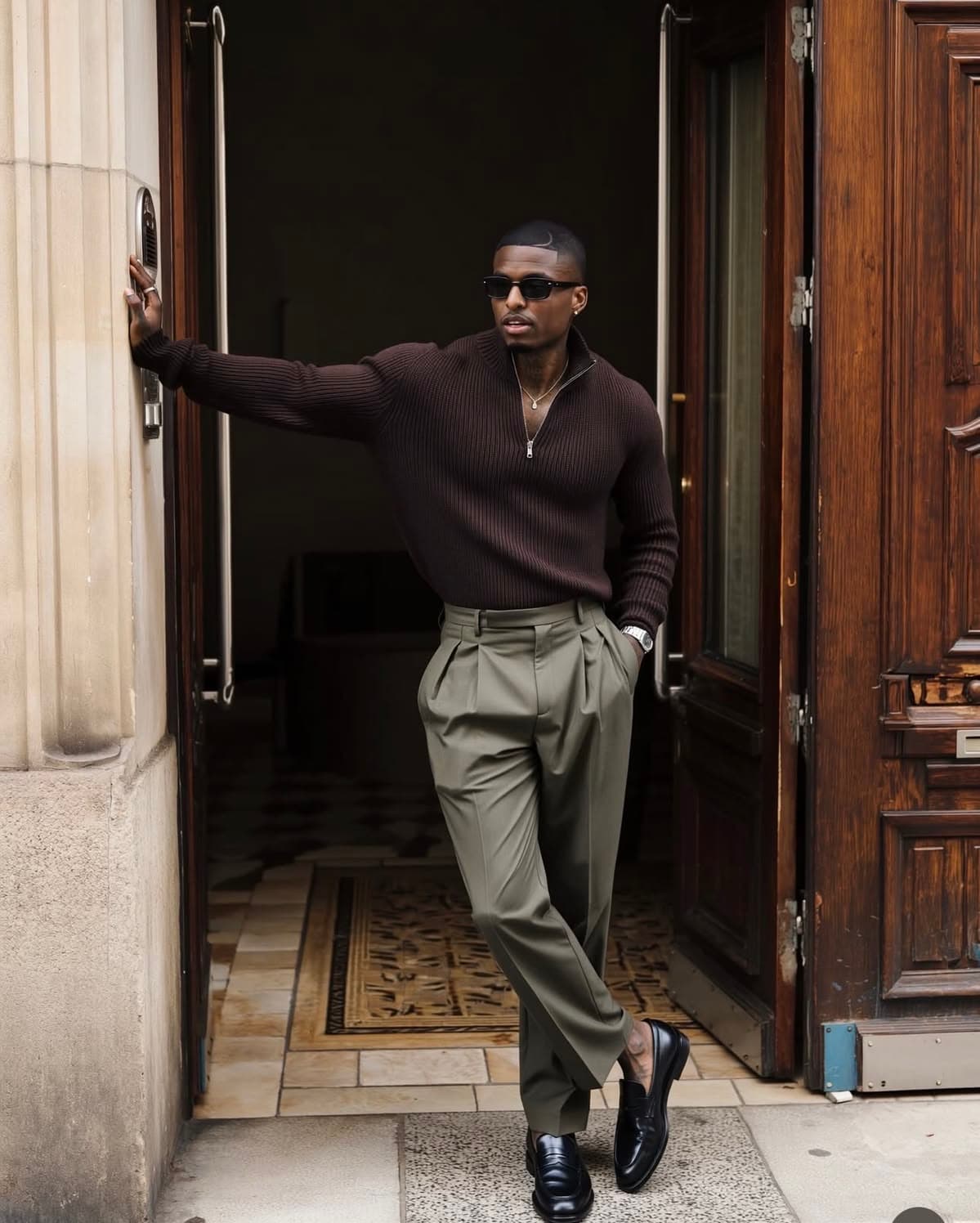A man in a brown half-zip knit in a panelled doorway