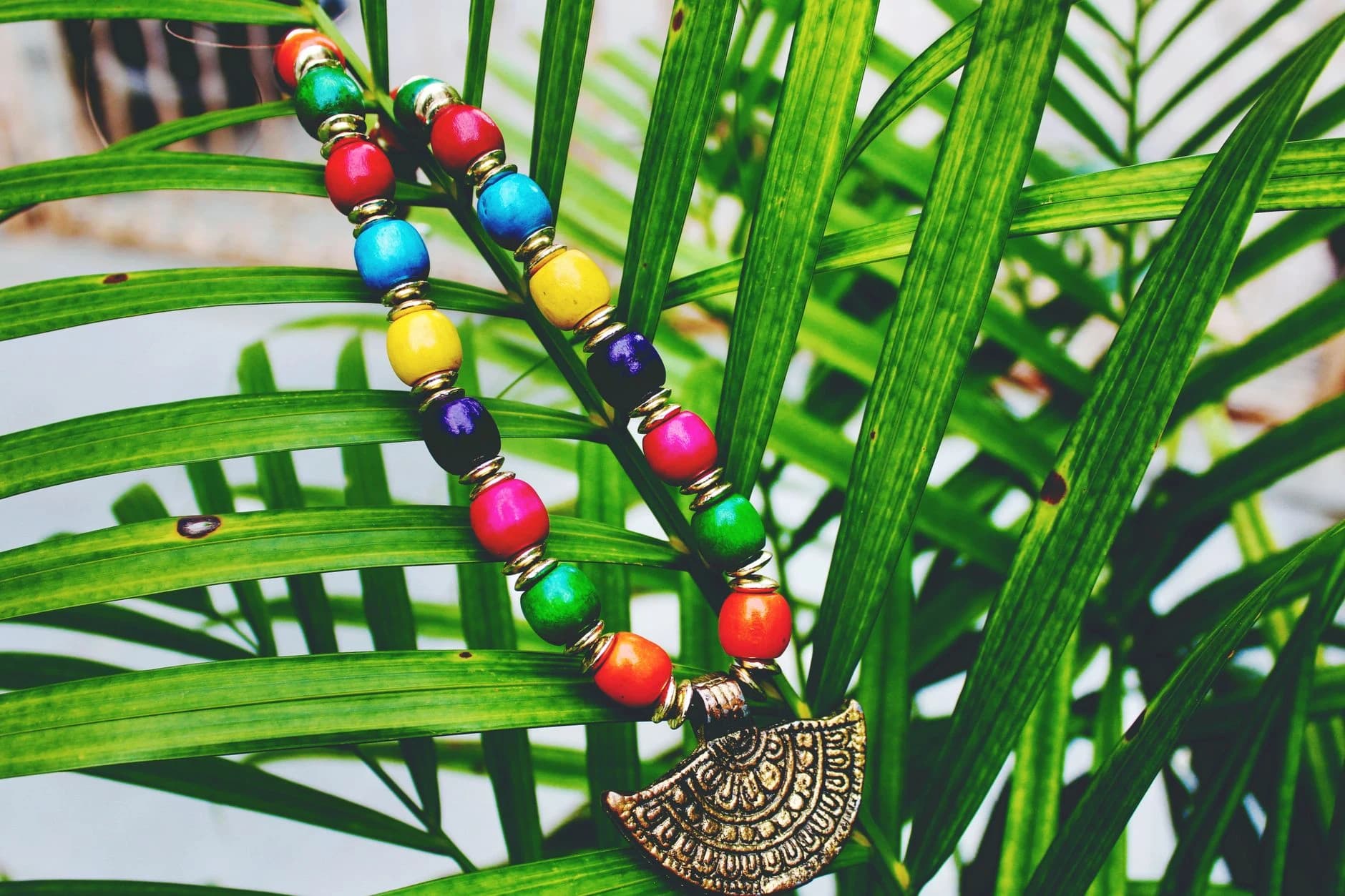 A strand of coloured beads with a carved gold pendant on palm fronds