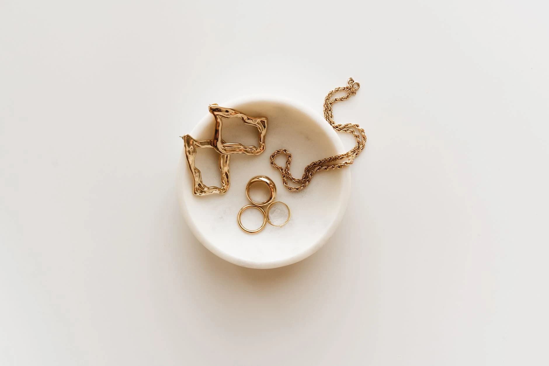 Three gold bands and a fine chain in a white ceramic dish