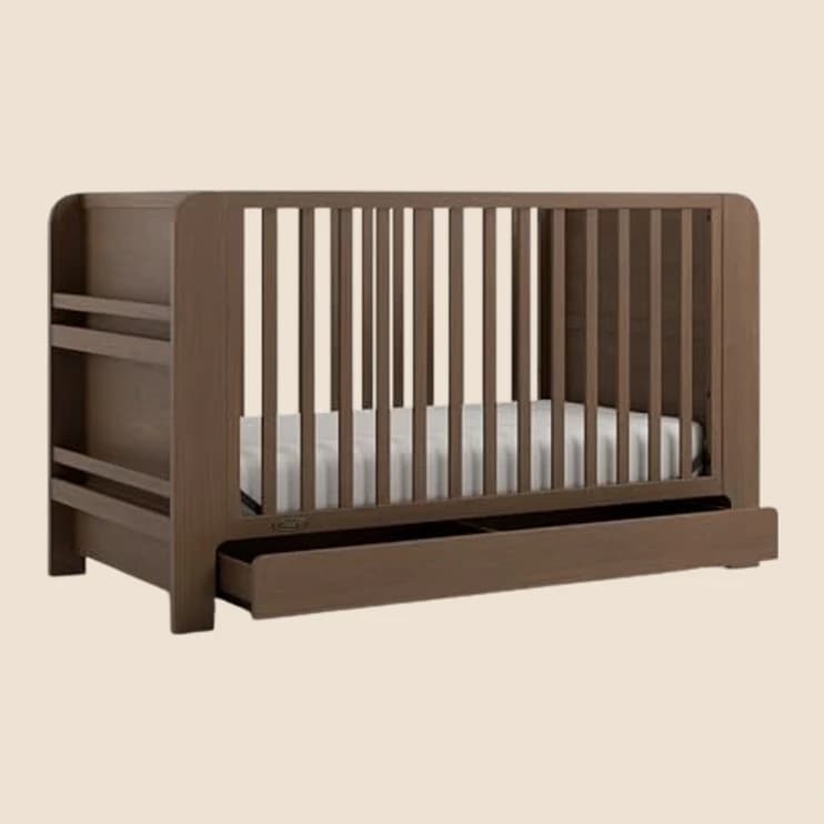 A dark wood convertible crib with a drop-side rail